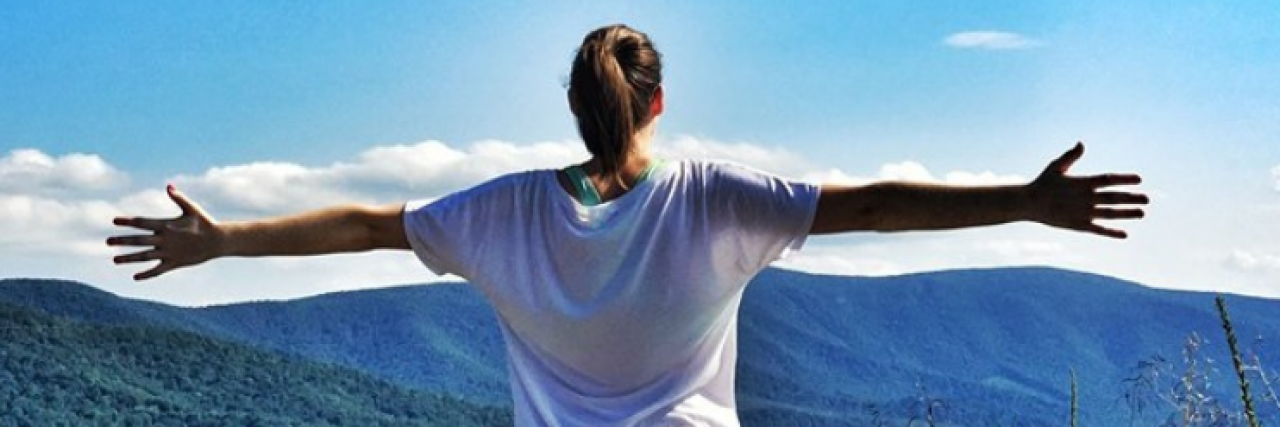 Woman standing with arms spread wide looking out over mountain view