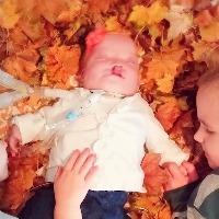 baby laying in fall leaves between two older siblings