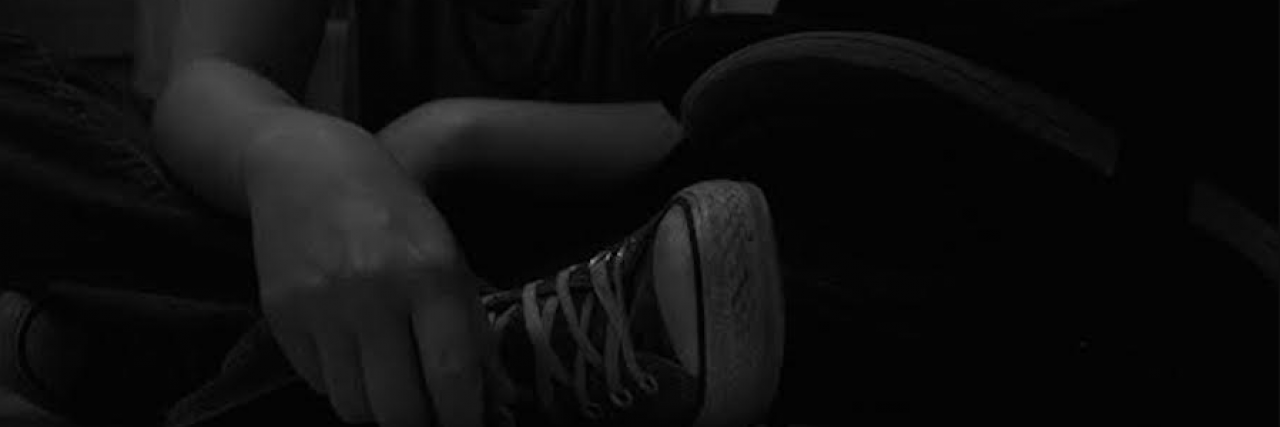Dimly lit close up photo of person sitting on the ground with their hand in front of their sneaker