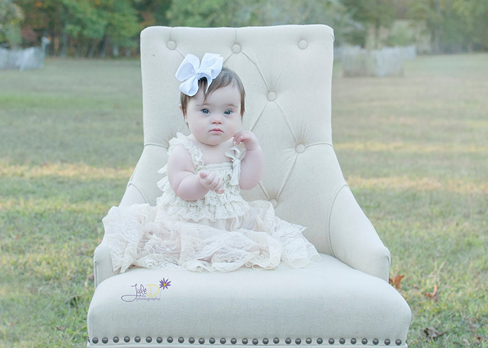 Baby with a bow sitting in chair in a park