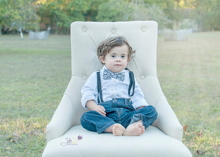 Baby wearing bow tie and suspenders sitting on a chair in a park