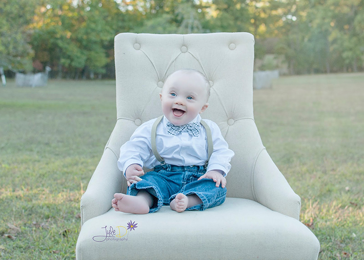 Baby wearing bow tie and suspenders sitting in chair outside