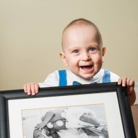 Young smiling boy holds up a picture of himself as a preemie.