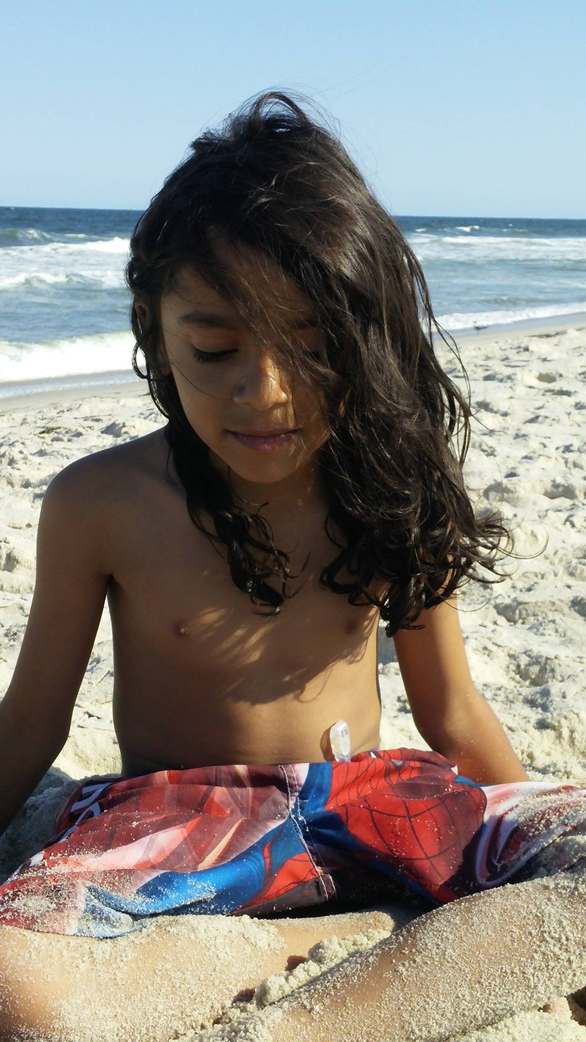 A young boy with long hair at the beach. 
