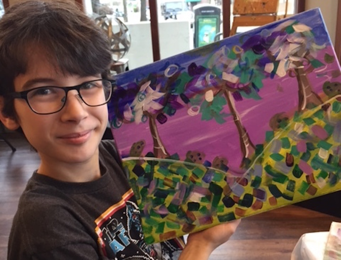 boy in glasses holding up colorful painting