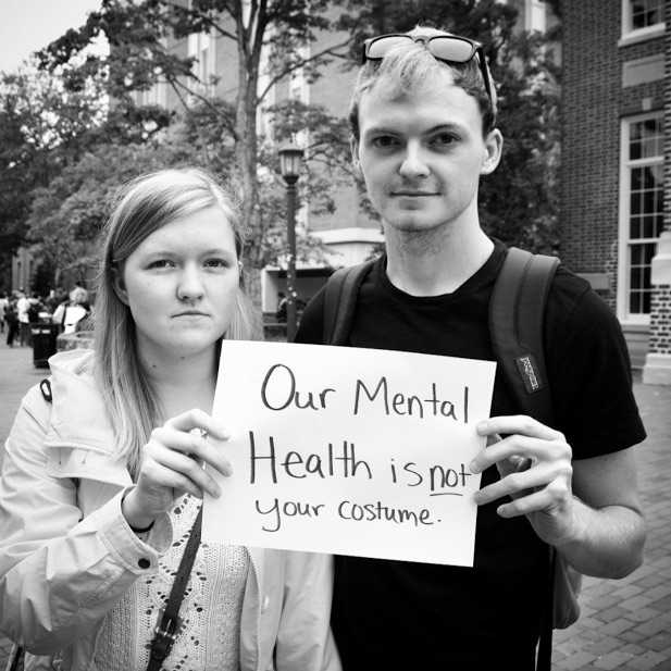 mental health advocates hold sign saying 'our mental health is not your costume'