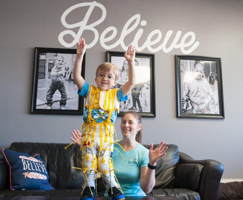 A boy with spina bifida standing with his hands in the air, smiling. 