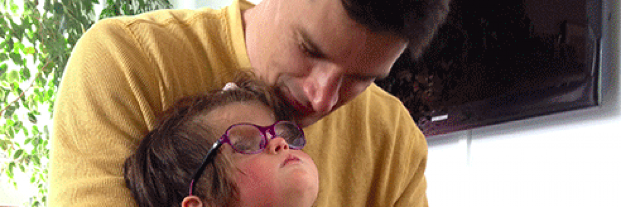 Dad smiles while holding young daughter on his lap, her face lifted towards his