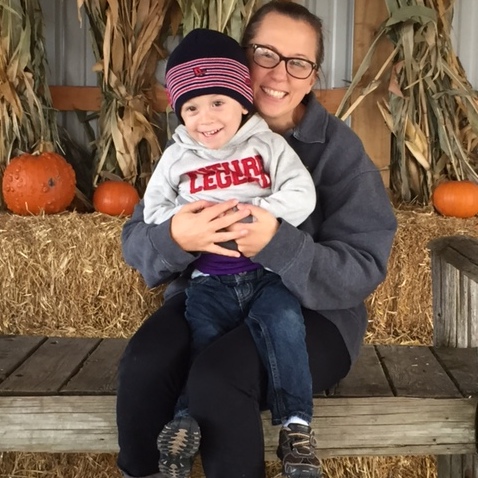 Sitting boy sits on his mom's lap in front of pumpkins. 