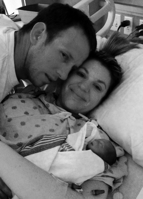 2 parents on a hospital bed next to their newborn baby