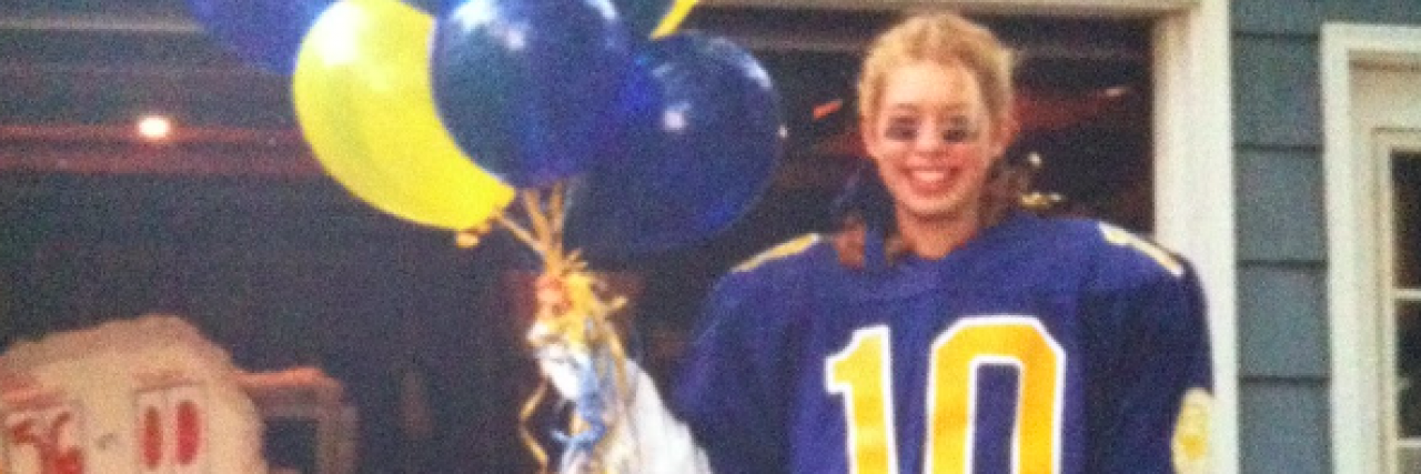 A young lady in a football player uniform holding matching colored balloons