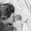 A mom kissing a new born baby laying in a hospital bed