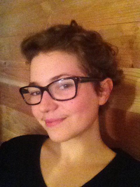 Woman wearing glasses, standing in front of wood wall