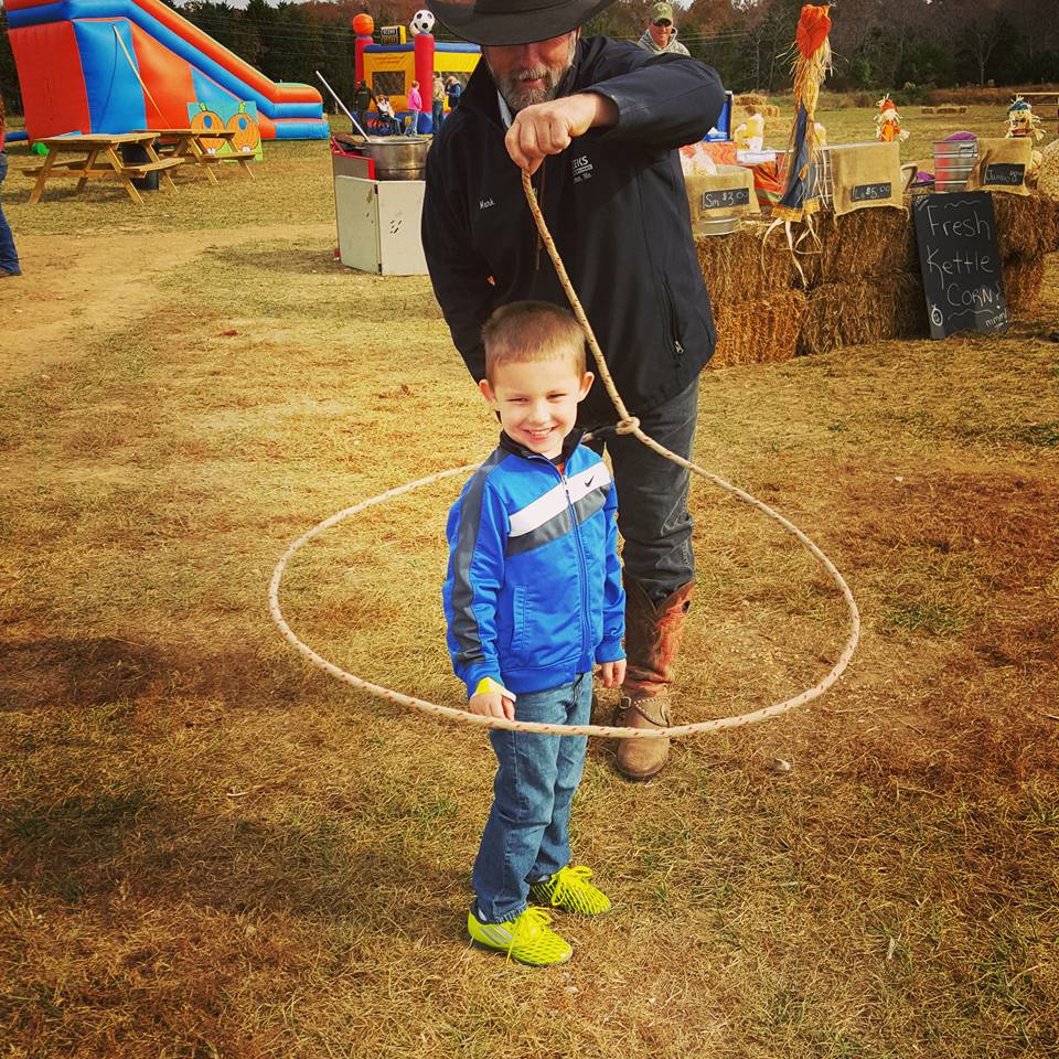 A cowboy swings a lasso around a little boy. 