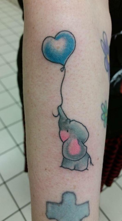 A tattoo of a gray elephant holding a blue heart-shaped balloon with its trunk