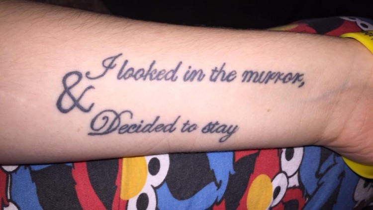 A tattoo of the words "I looked in the mirror, & Decided to stay" on a forearm