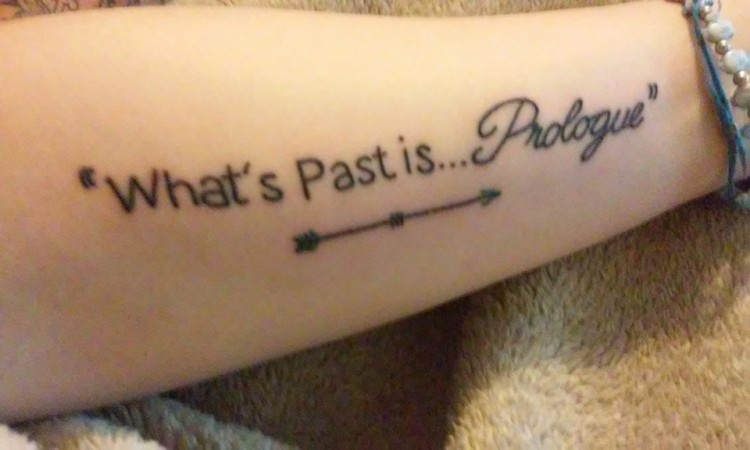 Tattoo on forearm that says, "What's Past is...Prologue" and an arrow underneath