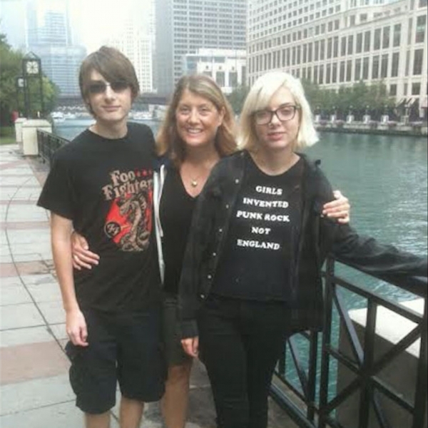 Three adults, one man and two women, embracing and smiling for the camera, in front of a bridge over water