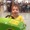 young boy smiling and playing on a ride at the mall