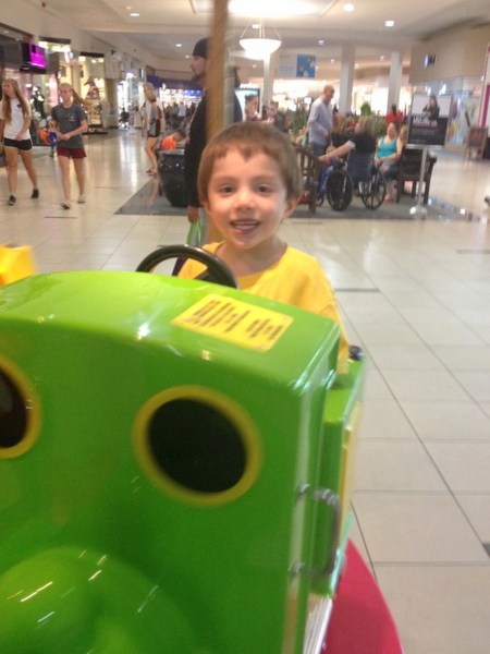 young boy with special needs smiling and playing on a ride at the mall