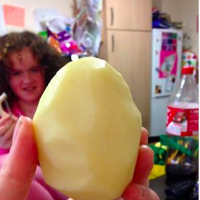 A closeup of a woman's hand holding a peeled potato with her daughter in the background