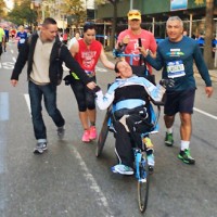Runners push man in broken wheelchair to the end of the race
