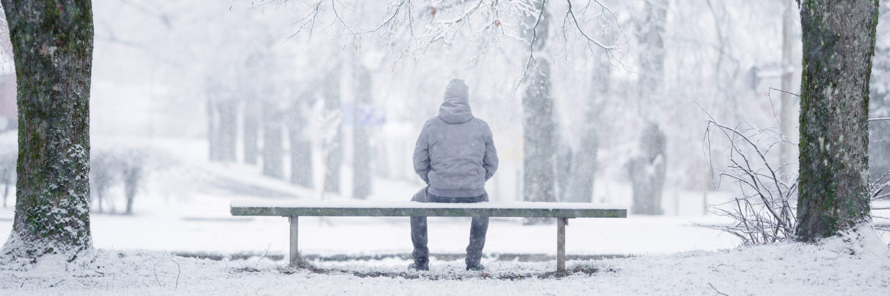person sits on bench with parka in a winter scene