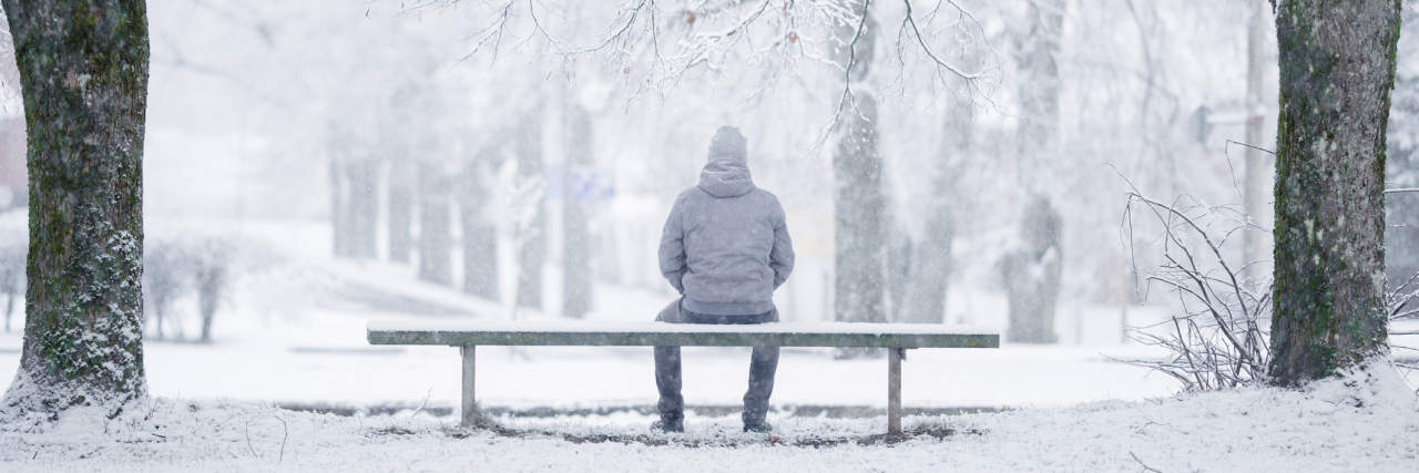 It's December and I Still Have Depression person sits on bench with parka in a winter scene