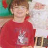 A small, smiling boy with glasses sitting on Santa's lap