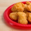 A serving of chicken nuggets on a red plate on a wood table top illuminated with window light.