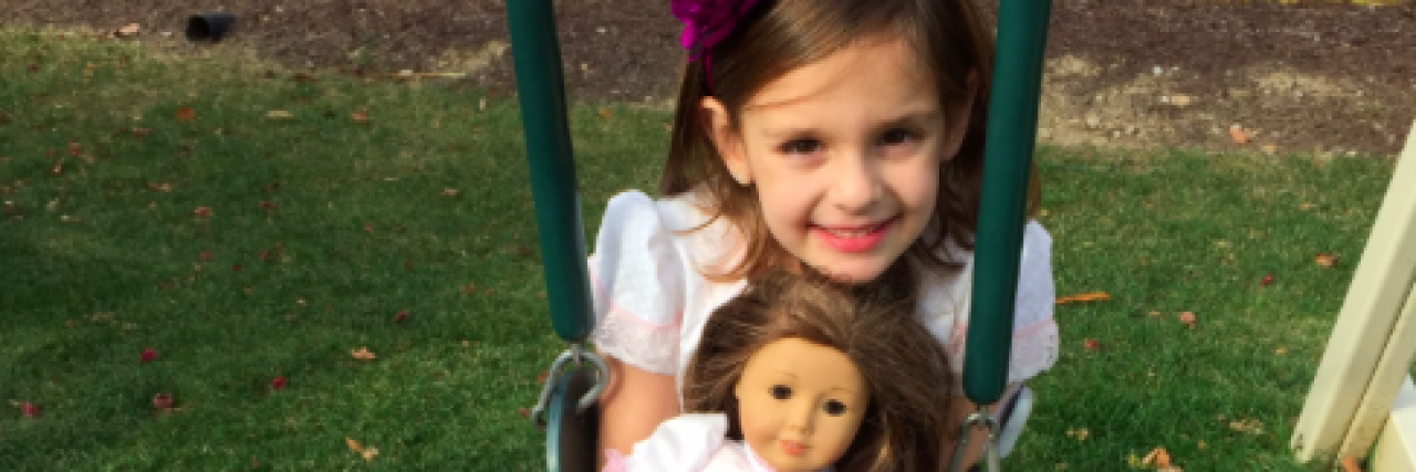 Young girl smiling on swing and holding an American Girl doll