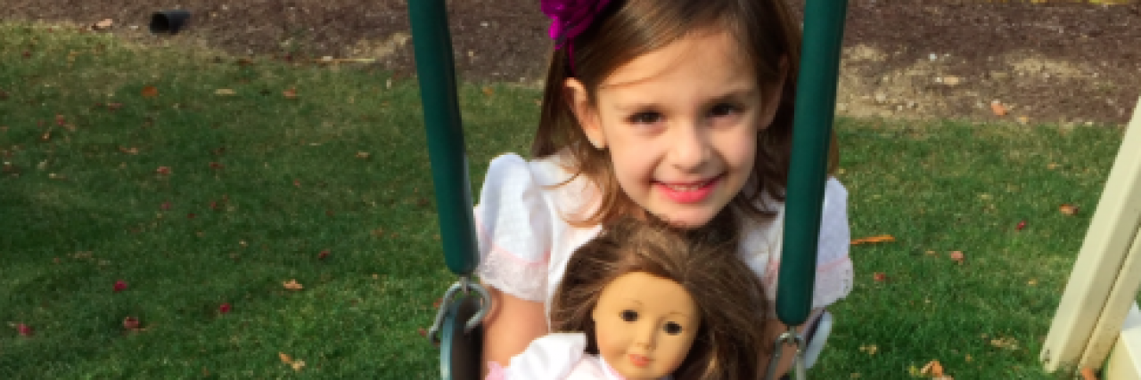 When I Gave My Daughter a Diabetes Kit for Her Dolls Young girl smiling on swing and holding an American Girl doll