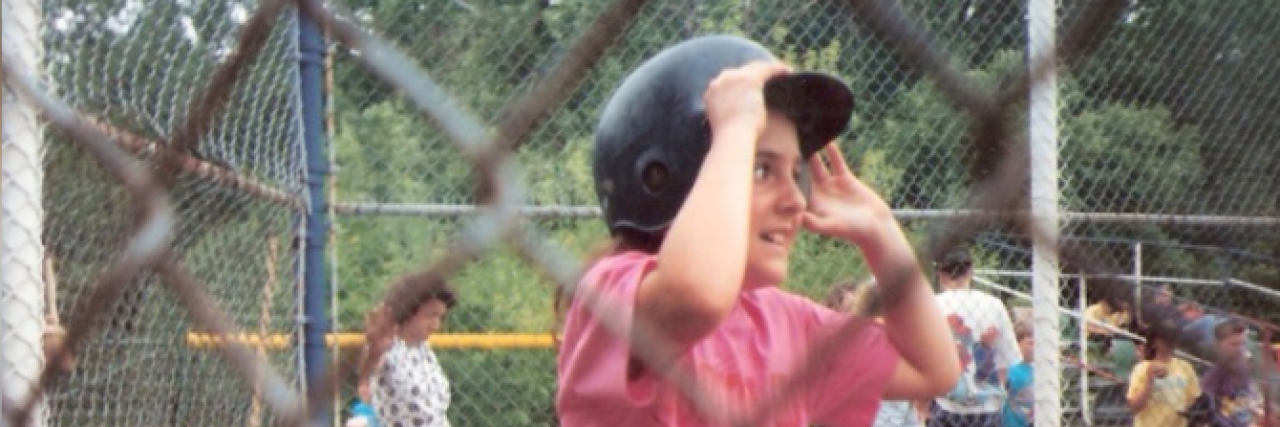 Young girl wearing a baseball helmet seen through a chain link fence
