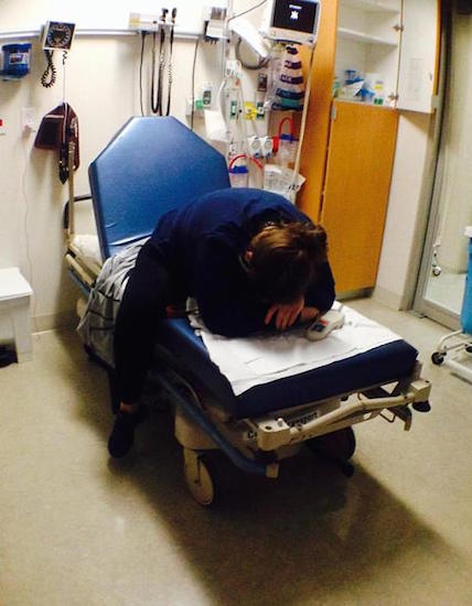 Woman on a hospital bed leaning over with her head on her hands