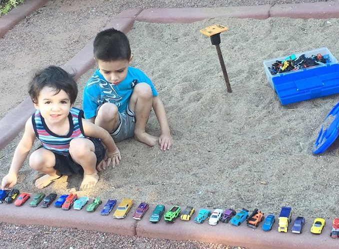 Two brothers playing in sandbox with toy cars