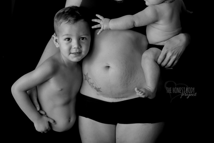 A mom shows off a tattoo on her stomach and holds her kids