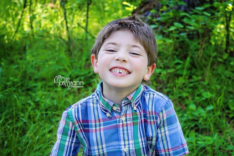 boy smiling in a plaid shirt with trees in the background