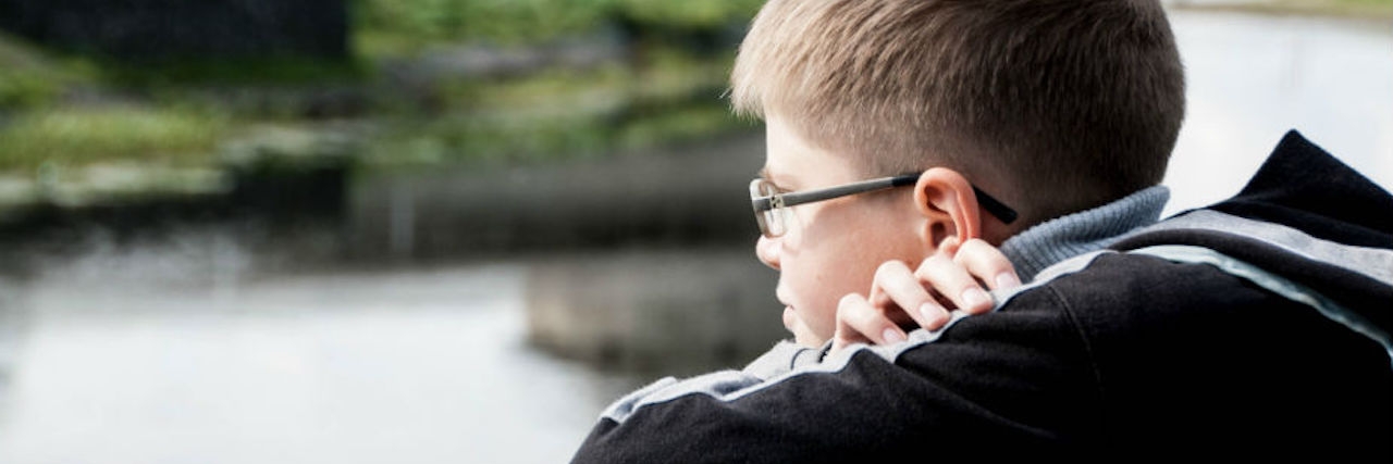 A boy with his head resting on his folded arms and looking at river