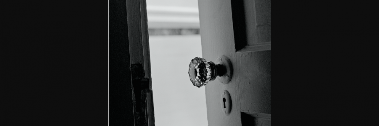 Black and white photo of door slightly open, with focus on door handle