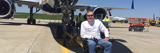 a man in a wheelchair in front of an airplane on a landing strip