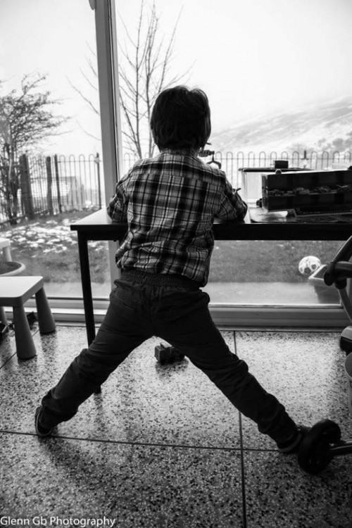 A young man from behind standing near a window. 