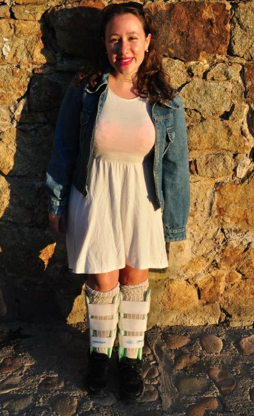 Woman in a white dress and denim jacket posing in front of a wall