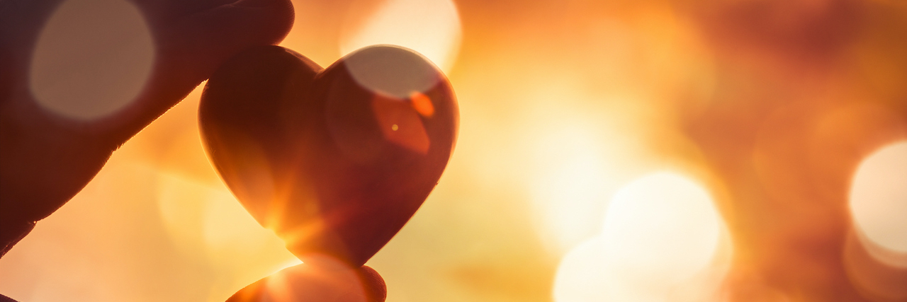 Messages to People With Depression, From Their Friends Close up of fingers holding heart against sparkling golden lights.