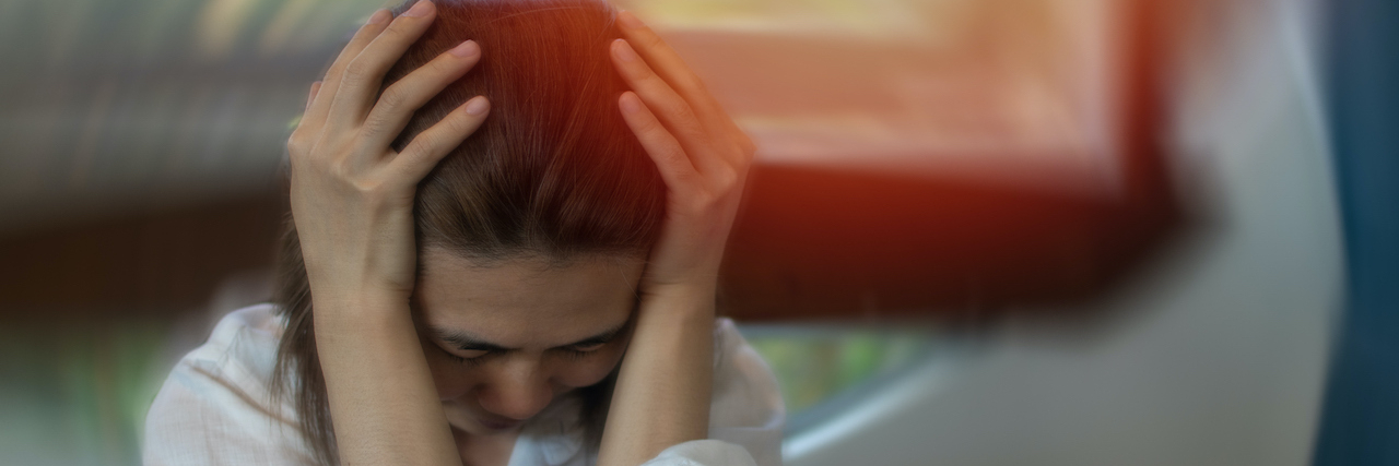 People Explain What Sensory Overload Feels Like Woman holding her head with eyes closed and room blurred behind her