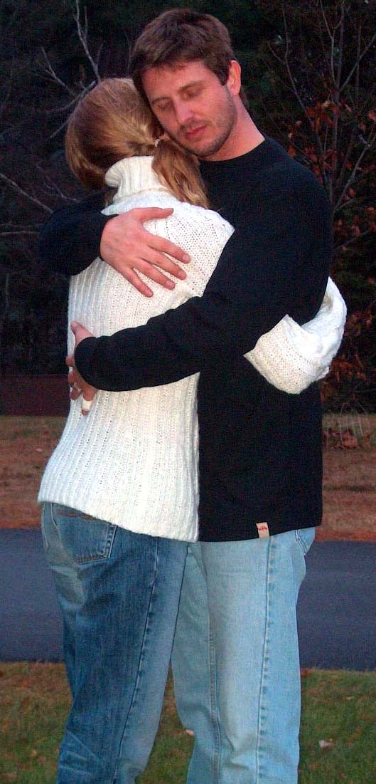 Couple hugging. The woman is wearing a white sweater, and the man is wearing a black sweater. Both of them are in jeans.