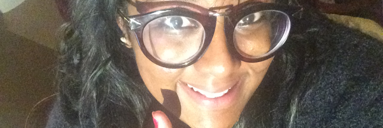 Woman of color wearing glasses and giving thumbs up