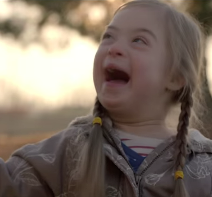 Small girl with pigtails holds adults' hand and smiles, while looking off to the side