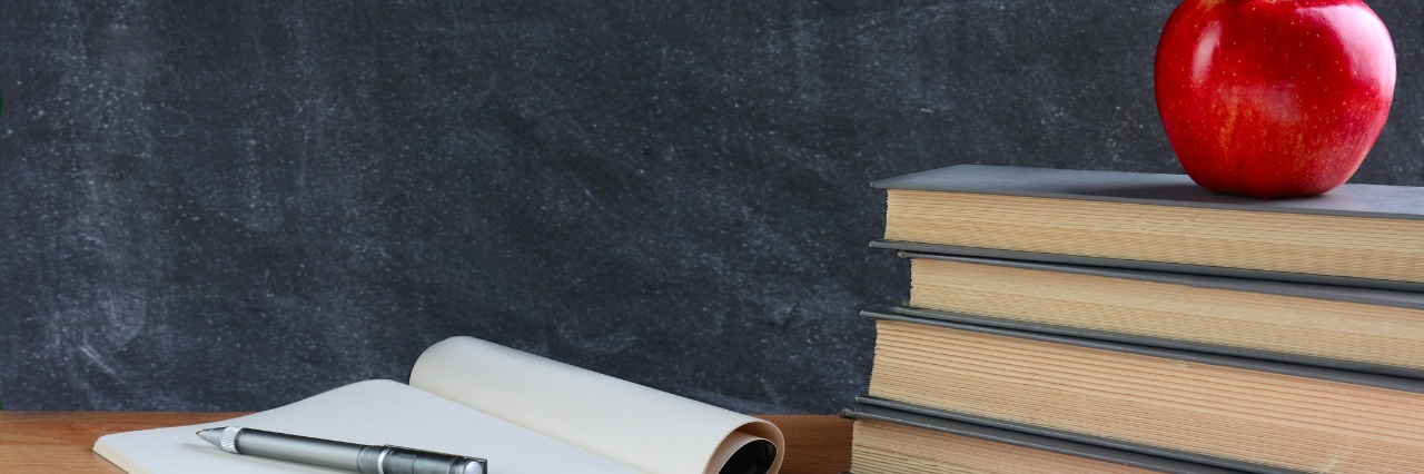 Secrets of Special Education Teachers Closeup of a teachers desk with books, paper and pen and a red apple in front of a chalkboard