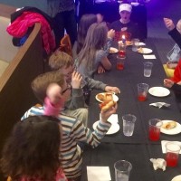 9-year-old boy having a birthday party -- he and his friends are sitting at a table, eating pizza and cheering as he begins to blow out the candle on his cupcake