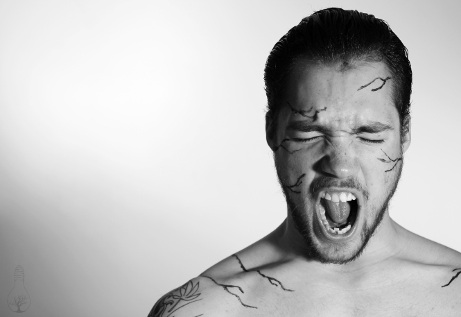 Man screaming, with black streaks on his face.